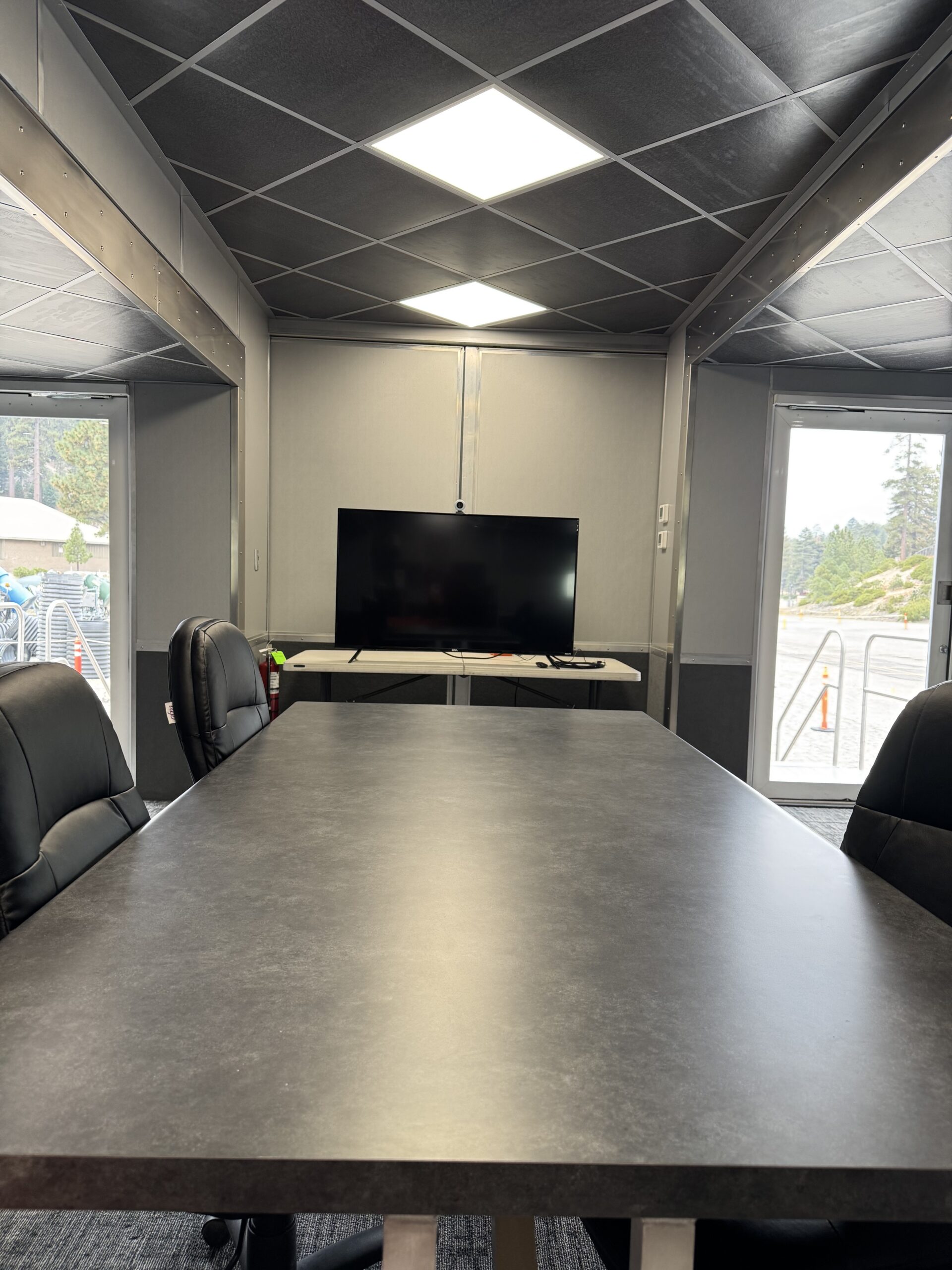 Interior of a mobile command unit with a conference table, operator seating, and a wall-mounted briefing display.