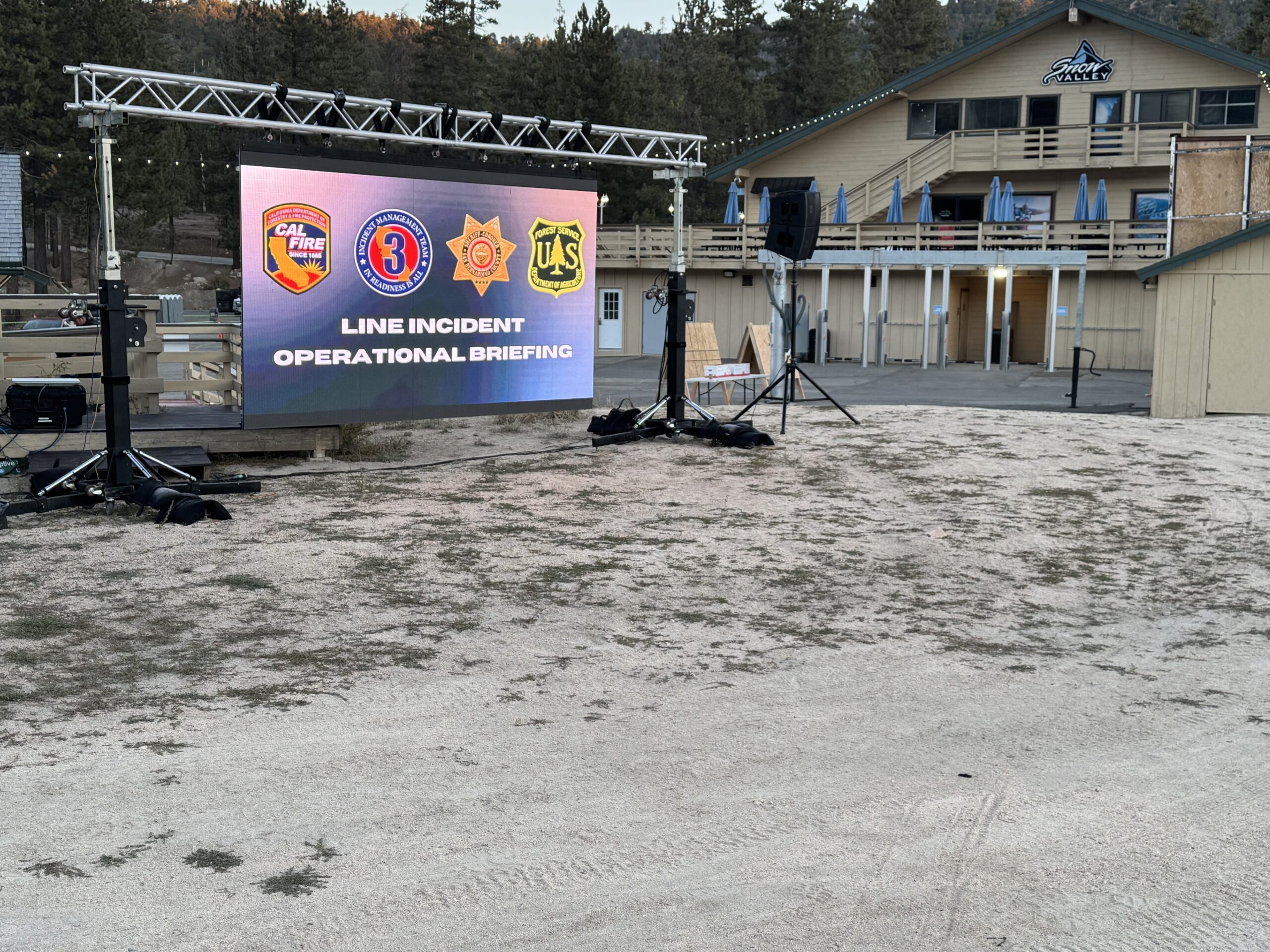 Large-format direct-view LED wall displaying a multi-agency line incident operational briefing slide at dusk.